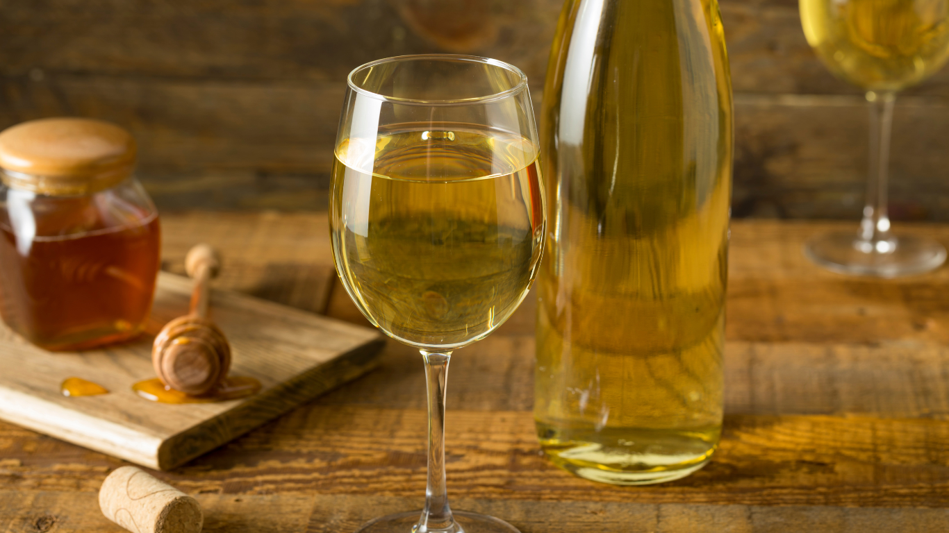 Bottle of mead with two glasses and jar of honey.